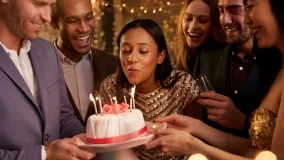 Young african american woman blowing out candles on birthday cake and celebrating with friends