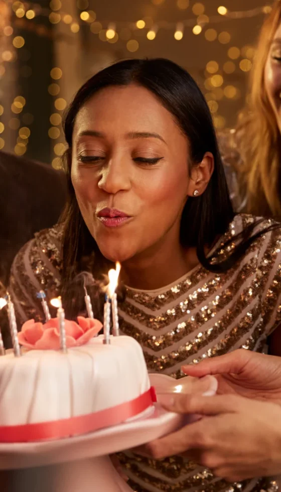 Young african american woman blowing out candles on birthday cake and celebrating with friends