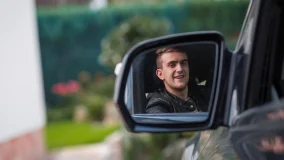 Young teen's reflection in driver's side mirror of his car wearing a seat belt and smiling