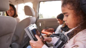 Mother turns around to see kids in their seat belts using tablets in the back of car