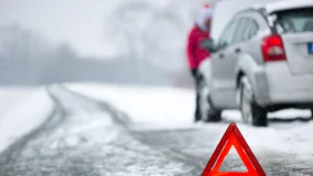 Winter snowy road and car breakdown and emergency warning triangle on road behind vehicle