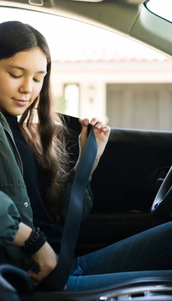 Teenage girl putting on her seatbelt getting ready to drive her car