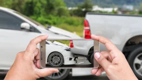 Woman holding smartphone and taking photo of her car accident