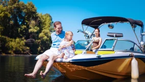 Dad and little girl sitting on the front of their boat with mom standing behind the steering wheel
