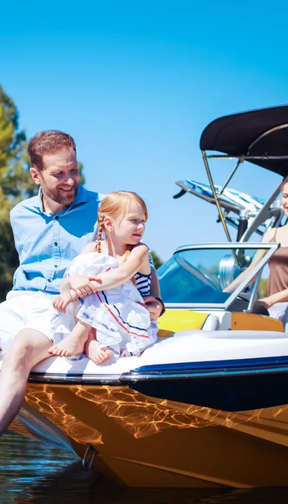 Dad and little girl sitting on the front of their boat with mom standing behind the steering wheel