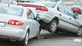 Two crashed silver cars and one stacked ontop the hood of the car in front