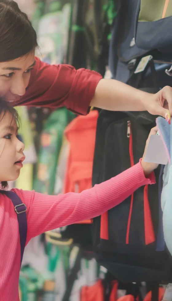 Young asian parent and little girl buying school backpack in store during tax-free holiday