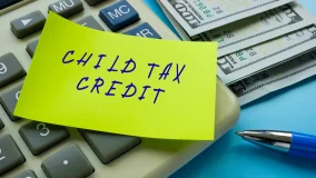 Yellow child tax credit handwritten note attached to manual calculator with paper money off to the side