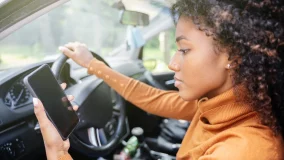 Young woman sitting in her car npt wearing a seat belt and checking her phone