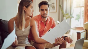 Stressed couple reviewing insurance documents with a laptop at home and upset feelings