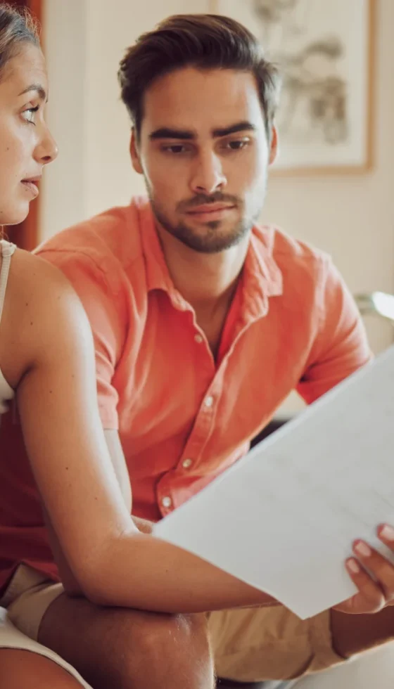 Stressed couple reviewing insurance documents with a laptop at home and upset feelings