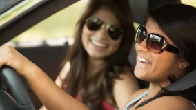 Young teenager and her friend having fun driving in the car wearing seat belts