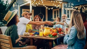 Family party gathered together at a table in the backyard with relatives and friends passing dishes and having fun.