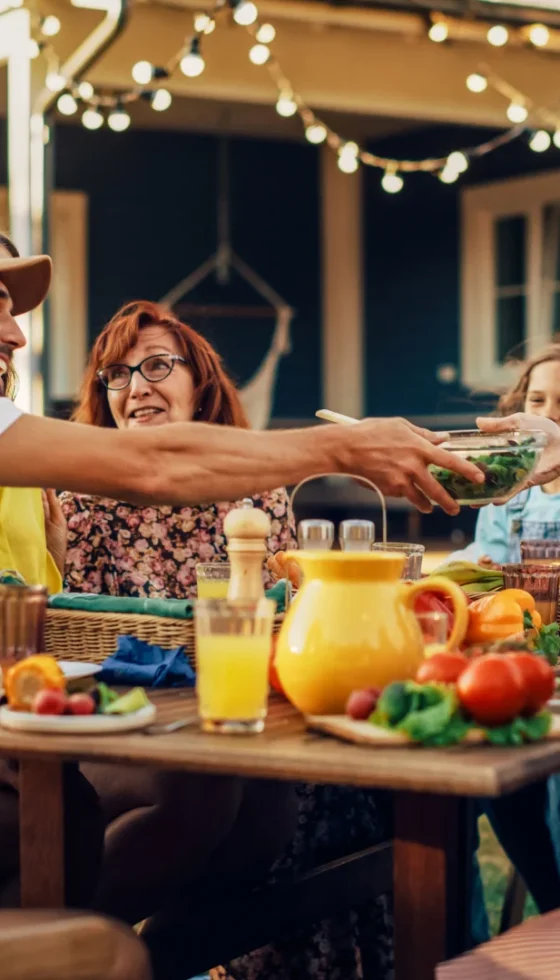 Family party gathered together at a table in the backyard with relatives and friends passing dishes and having fun.