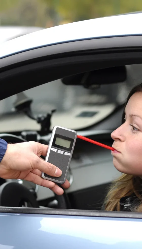 Young female driver being subject to test for alcohol content by police officer with use of breathalyzer.