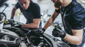 Cropped image of two male mechanics in uniform looking under the car hood and changing the oil