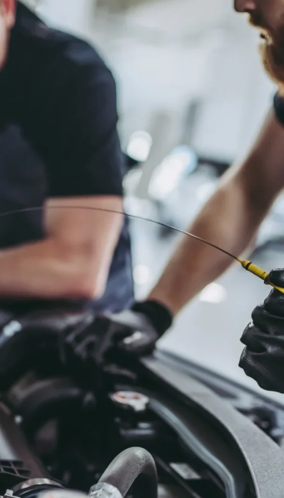 Cropped image of two male mechanics in uniform looking under the car hood and changing the oil