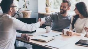 Happy young couple meeting with their insurance agent shaking hands and reviewing policy documents.