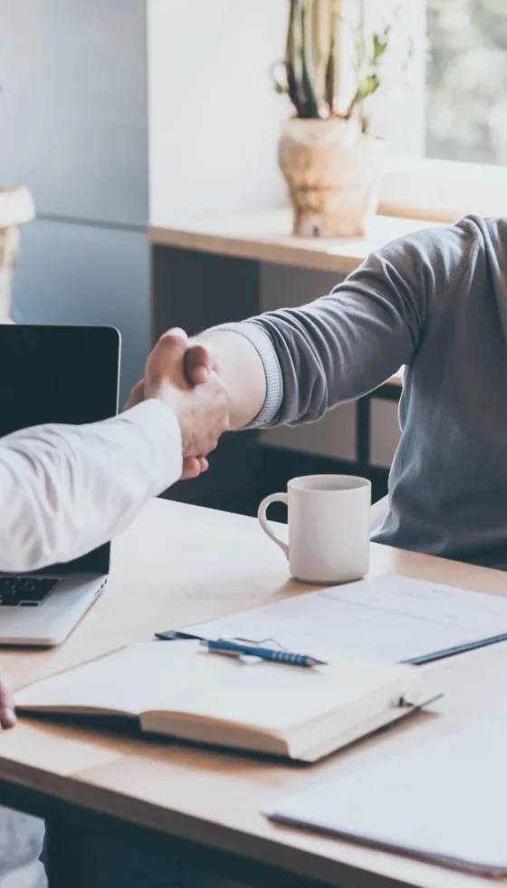 Happy young couple meeting with their insurance agent shaking hands and reviewing policy documents.