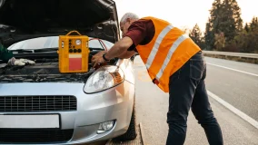 Two roadside assistance workers in towing service trying to start car engine with jump starter and energy station with air compressor.