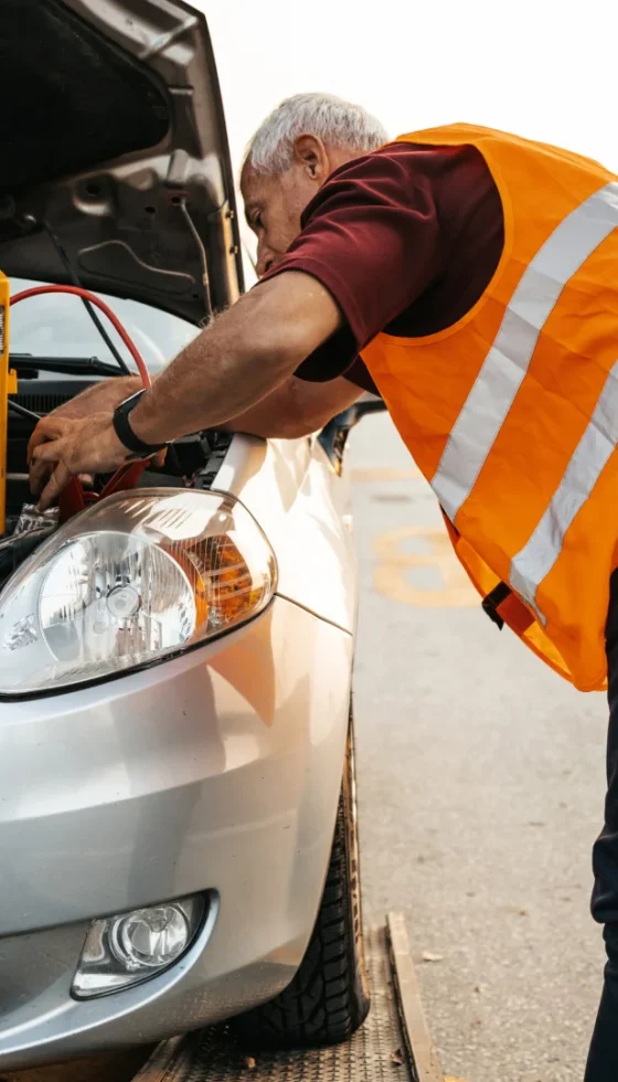 Two roadside assistance workers in towing service trying to start car engine with jump starter and energy station with air compressor.