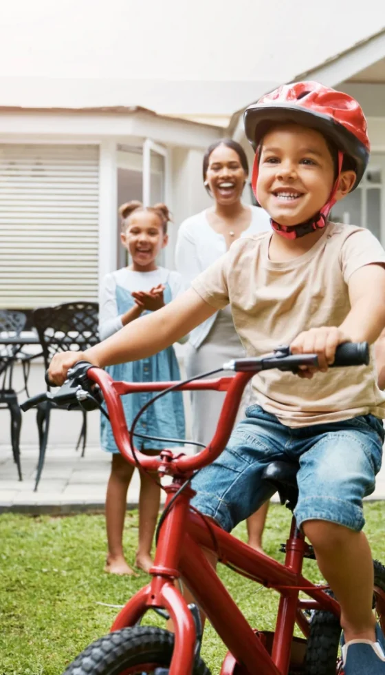 Dad and family teaching young son to ride while wearing a helmet for safety in their family home and life moment.