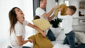 Young confident parents laughing with their children and playing with pillows on the bed.