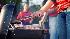 Man grilling in backyard with friends having a fun summer BBQ party.