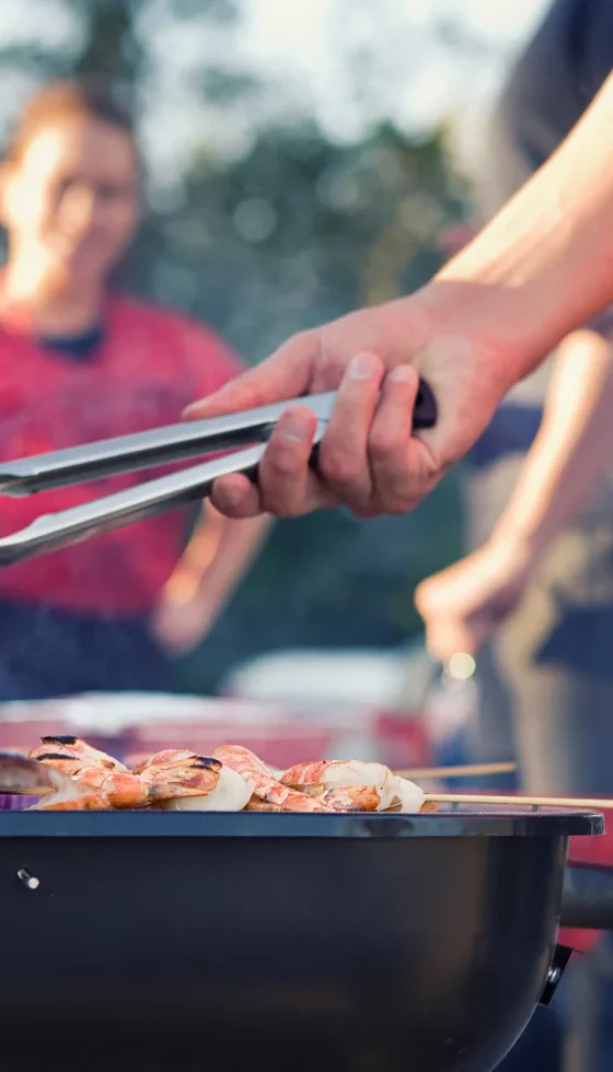 Man grilling in backyard with friends having a fun summer BBQ party.