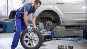 Young male mechanic with car tire in service center checking and maintaining the vehicle for safe driving