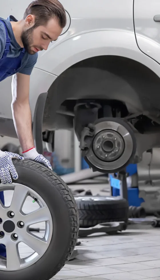 Young male mechanic with car tire in service center checking and maintaining the vehicle for safe driving