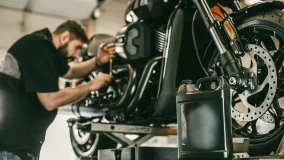 Male mechanic changing the oil and doing routine maintenance on a motorcycle up on a lift.