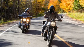 Group of friends riding motorcycles and wearing helmets on a country road in the fall.