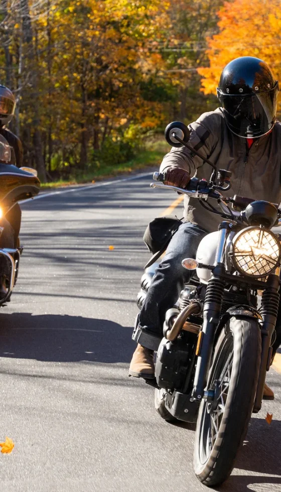 Group of friends riding motorcycles and wearing helmets on a country road in the fall.