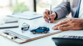 Man signing new car insurance document writing signature with car keys on table