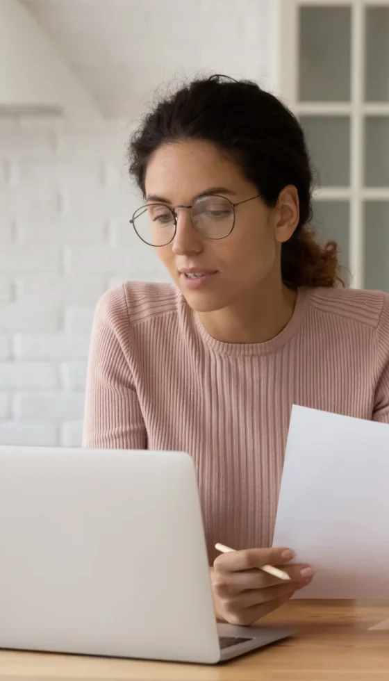 Young hispanic female at home reviewing her auto insurance policy on computer and paper documents