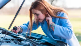 Woman having car trouble and looking under the open hood and on the side of the road safe from traffic