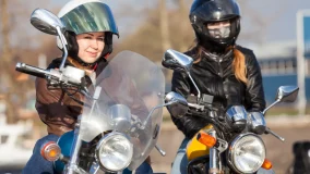Two female bikers wearing helmets with classic and street style bikes in city.