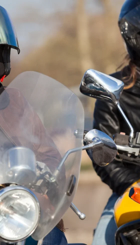 Two female bikers wearing helmets with classic and street style bikes in city.