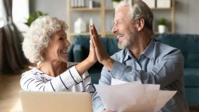 Excited older couple giving high five celebrating buying a new car with their tax refund