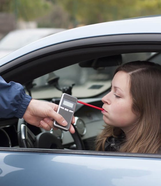 Young woman blowing into a breathalyzer after getting pulled over by a police officer - cheap SR22 insurance.