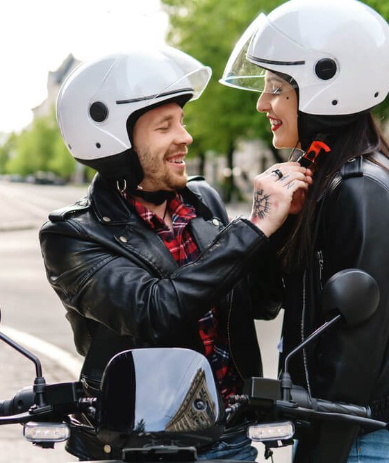 A couple gets ready for a motorcycle ride, the man adjusts the woman's helmet - cheap motorcycle insurance.