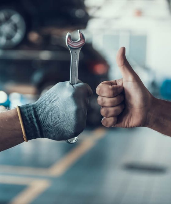 Mechanic giving a thumbs-up while holding a wrench next to a driver who brought his car for repair to his nearby local repair shop - Acceptance, cheap auto insurance