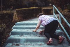 An elderly woman slips and falls on the stairs outside someone's home.
