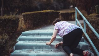 An elderly woman slips and falls on the stairs outside someone's home.