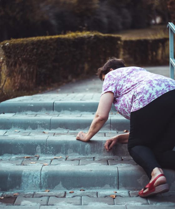 An elderly woman slips and falls on the stairs outside someone's home.