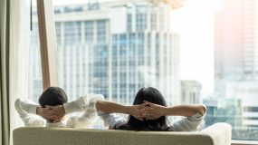 Man and woman seen from behind relaxing on couch and looking out the window of their condo - cheap condo and home insurance.