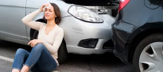 injured woman holding her head sitting against her car bumper