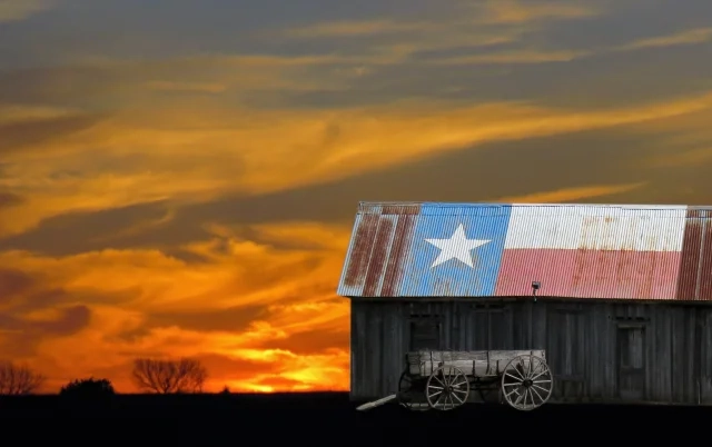 Sunset with abandoned barn and buckboard wagon. Barn has a Texas flag painted on the tin roof – El Campo, cheap car insurance in Texas