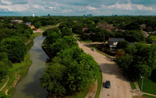 An aerial drone photo of a sunny summer day in Plano Texas next to a river park with a car driving on the street.